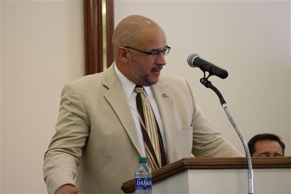 Phillip Brown wears a tan suit with a patterned tie while speaking from behind a podium during Baccalaureate. 